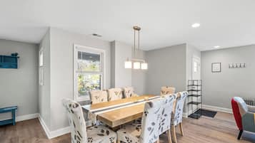 A dining area with a wooden table and floral-patterned chairs, a pendant light, and a window with blinds.