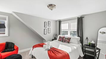 A bedroom with a bed, a chair, a nightstand, a mirror, and a window with curtains.