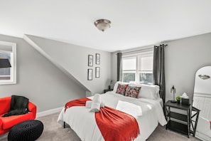 A bedroom with a bed, a chair, a nightstand, a mirror, and a window with curtains.