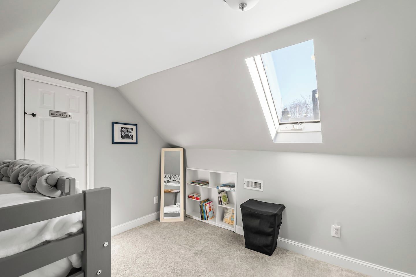 A child's bedroom with a bunk bed, a skylight, a bookshelf, and a trash bin.