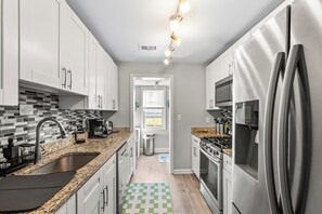 A modern kitchen with white cabinets, a granite countertop, stainless steel appliances, and a checkered floor mat. - Pet-Friendly Family Home Near DC | Sleeps 16 (Hyattsville)