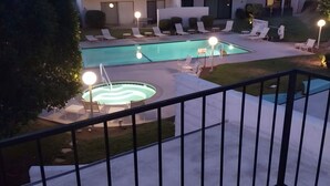 A swimming pool area with lounge chairs and a hot tub, surrounded by a well-maintained lawn and a building in the background. - 2-bedroom condo in fantastic Cathedral City with AC (Cathedral City)
