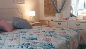 A bedroom with a floral bedspread, a nightstand with a lamp, a dresser with drawers, and a window with a view. - 2-bedroom condo in fantastic Cathedral City with AC (Cathedral City)
