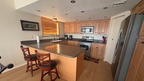 Una cocina moderna con armarios de madera, un refrigerador de acero inoxidable, un horno empotrado y una isla grande con taburetes de bar.