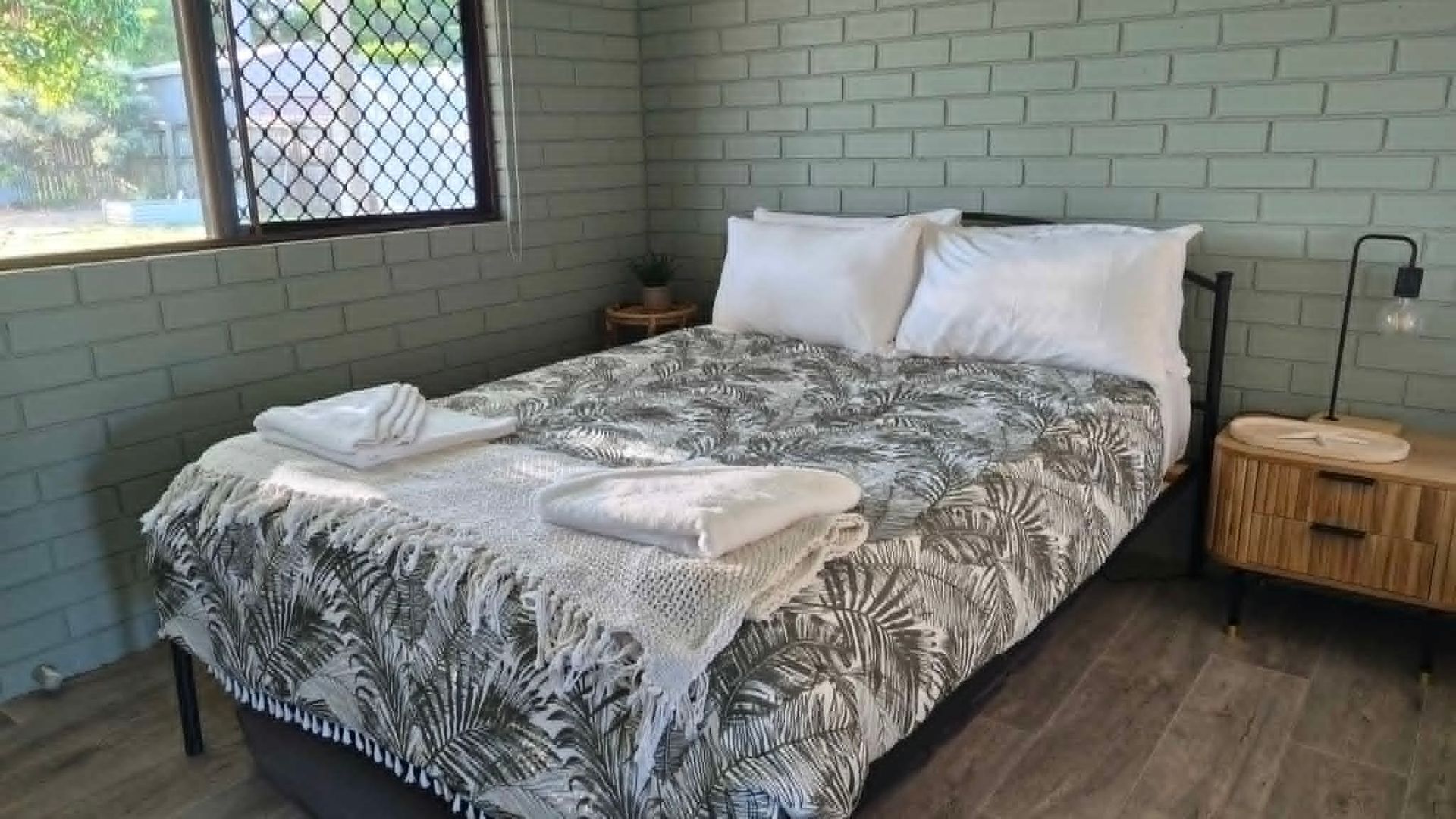 Une chambre à coucher avec un lit, une table de chevet, une lampe et une fenêtre donnant sur un beau paysage.