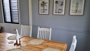 Un comedor con mesa de madera, sillas blancas y individuales tejidas.