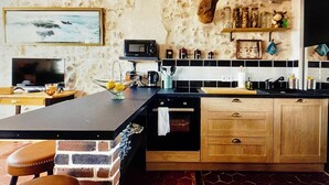 Eine Küche mit einer Holzeinrichtung, einer Mikrowelle und einer Kaffeemaschine. An der Wand hängt ein Bild und es gibt ein Regal mit Gläsern.