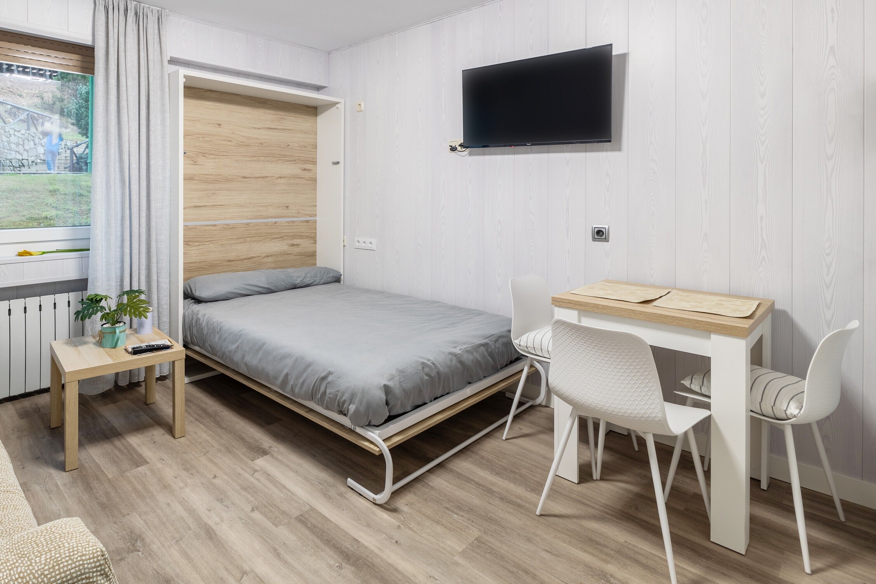 Una habitación con una cama, un escritorio, una silla, un televisor y una ventana con cortinas.
