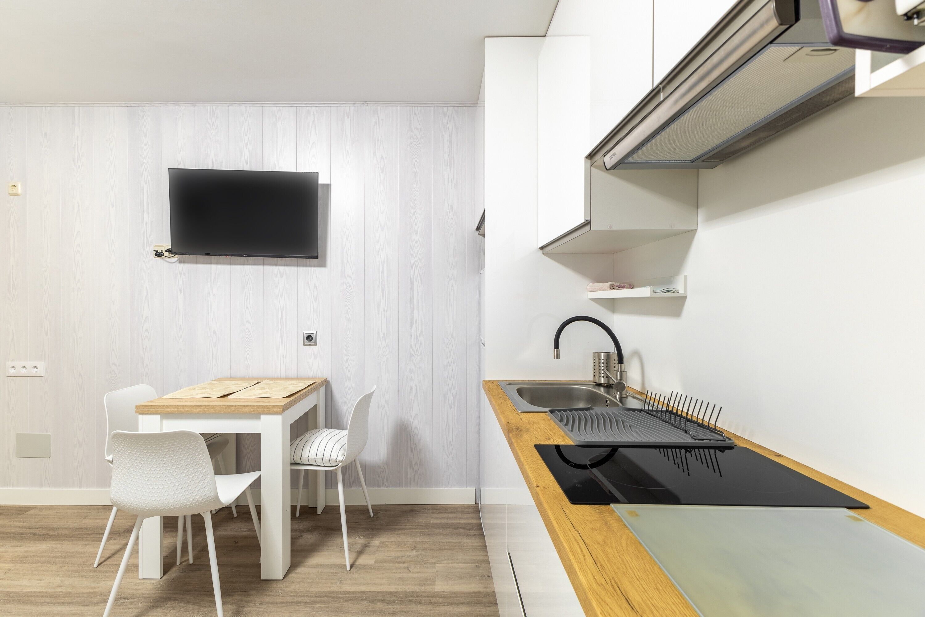 Una cocina moderna con una mesa de madera, sillas blancas, una encimera negra y una estufa empotrada.
