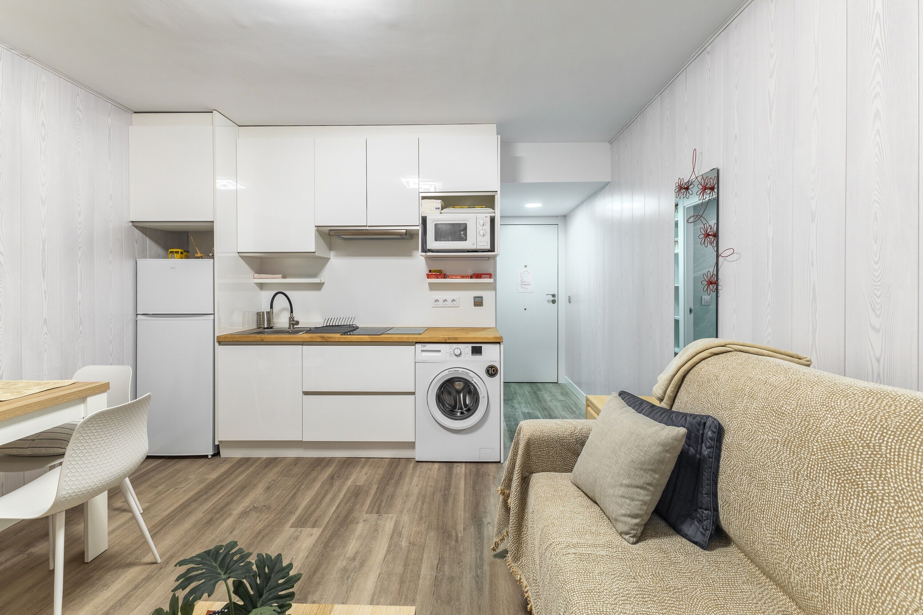 Un espacio habitable compacto con kitchenette, lavadora, comedor y sofá.