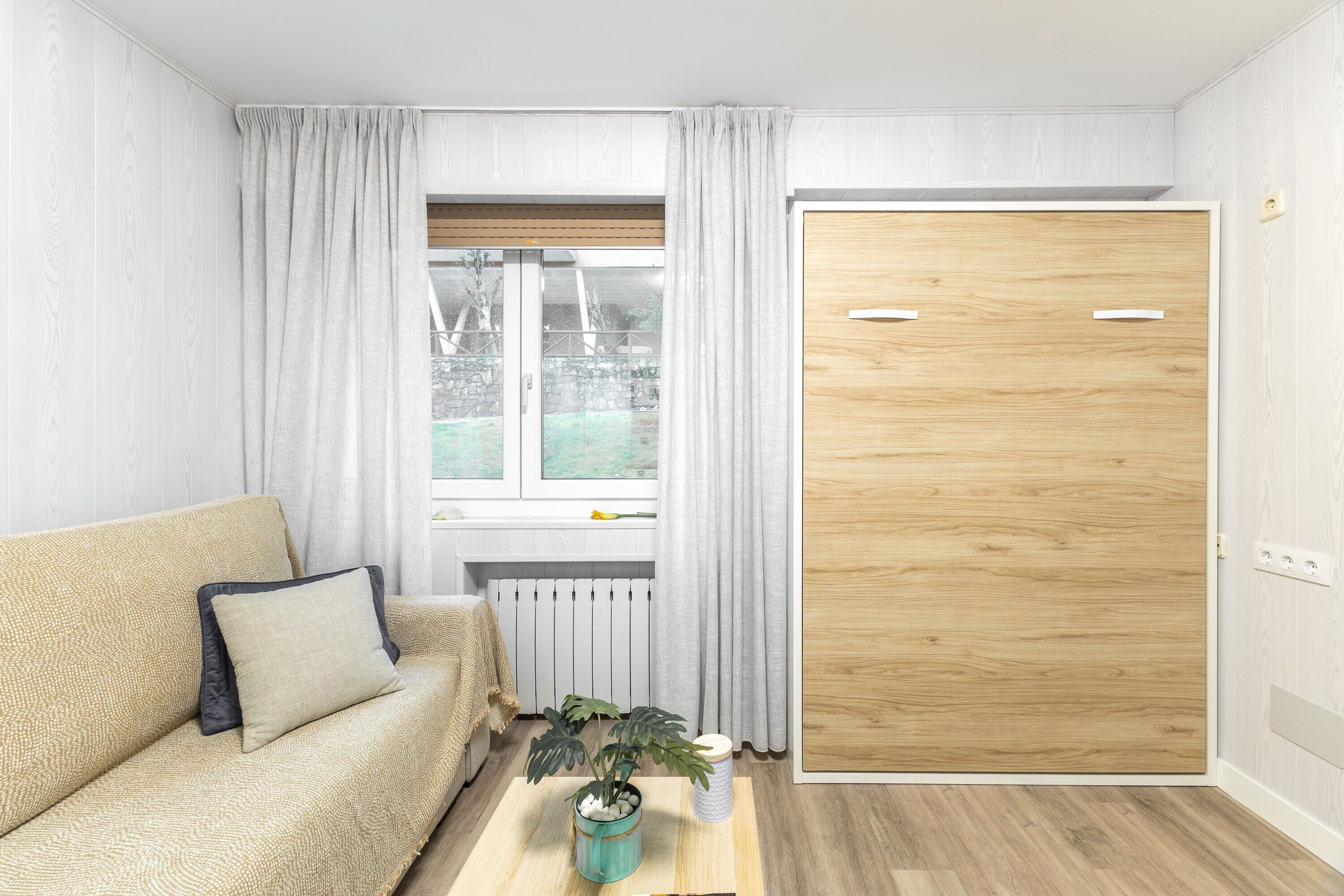 A modern room with a sofa, a wooden door, a window with curtains, and a radiator.