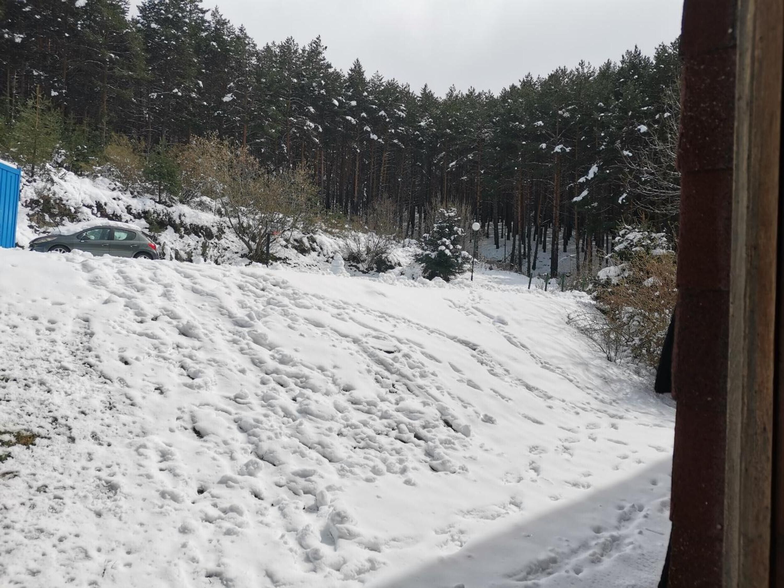 Eine verschneite Landschaft mit einem am Hang geparkten Auto und einem Wald im Hintergrund.