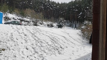 Eine verschneite Landschaft mit einem am Hang geparkten Auto und einem Wald im Hintergrund.