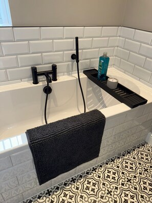 Un baño moderno con una bañera blanca, una toalla negra y baldosas de suelo estampadas.