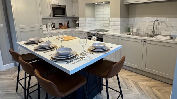 Uma cozinha moderna com ilha central, luminárias pendentes e padrão de piso em herringbone.