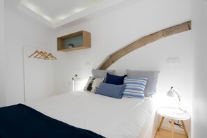 A bedroom with a bed, a bedside table with a lamp, a wooden shelf above the bed, and a coat rack. - Casa Castelo 1 - Work or Relax in the historic heart of Lisbon! (Lisboa ciudad)