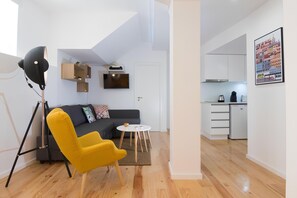 Ein modernes Wohnzimmer mit einer Couch, einem gelben Sessel, einer Stehlampe, einem kleinen Tisch und einer Küchenzeile mit Schränken und einem Kühlschrank.