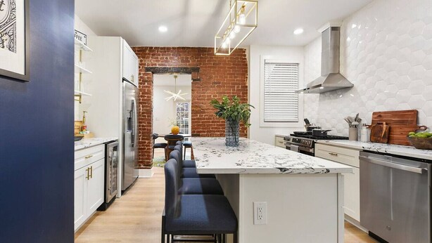 A modern kitchen with a central island, white cabinetry, a brick accent wall, and stainless steel appliances. - Rooftop Deck | 3 King Suites | Soaker Tub (Pittsburgh)