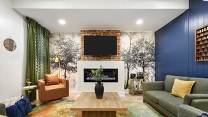 A living room with a fireplace, sofas, a coffee table, and a TV mounted on the wall. - Rooftop Deck | 3 King Suites | Soaker Tub (Pittsburgh)