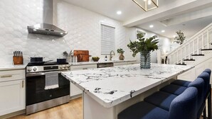 A modern kitchen with a central island, stainless steel appliances, and a hexagonal tile backsplash. - Rooftop Deck | 3 King Suites | Soaker Tub (Pittsburgh)