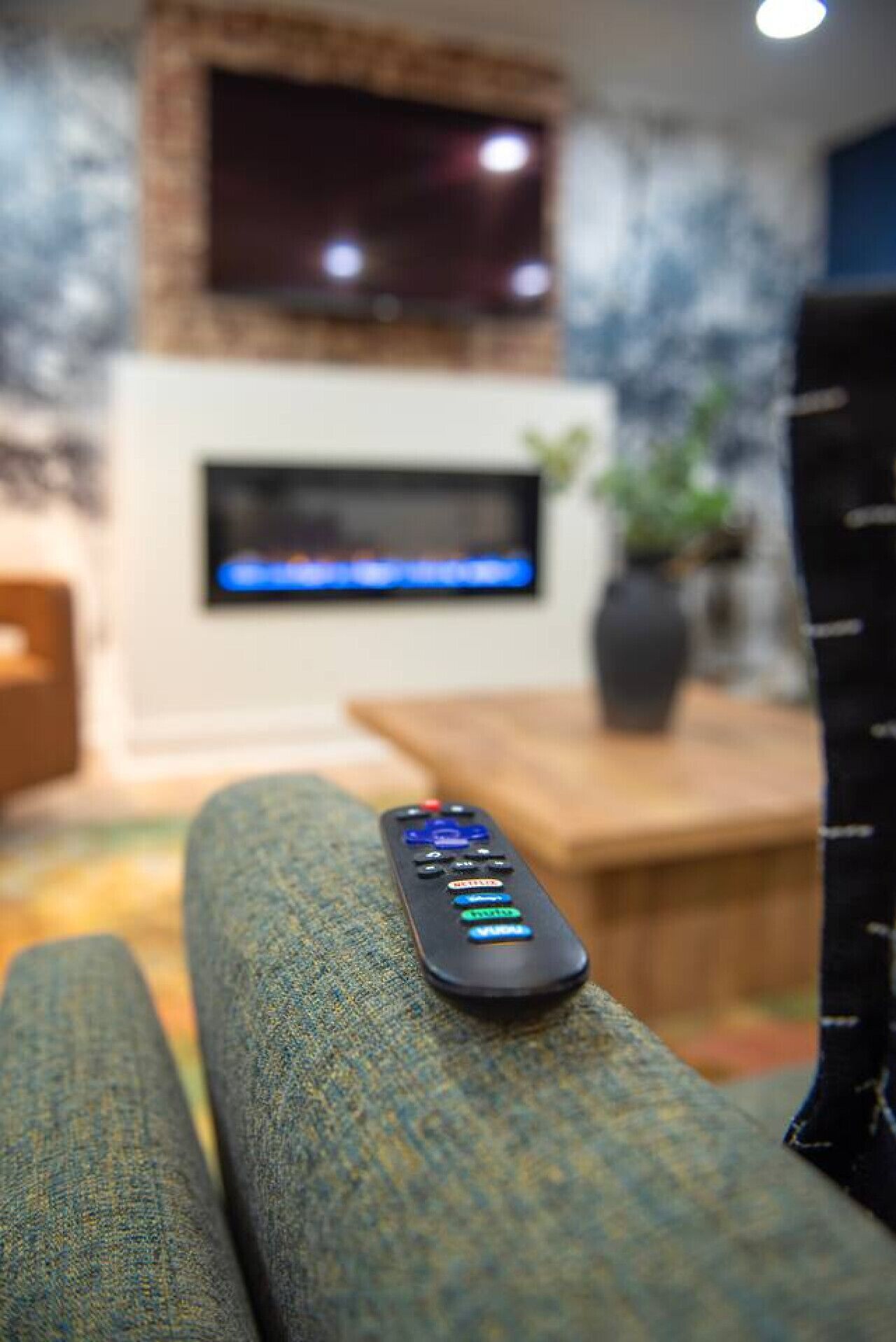 A remote control on a textured sofa in a living room with a fireplace, a television, and a plant.