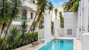 Ein moderner Poolbereich mit klarem, blauem Pool, umgeben von Palmen und einem weißen Gebäude mit Balkonen.