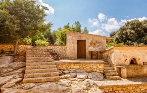 Una escalera de piedra conduce a un pequeño edificio con puerta de madera, rodeado de follaje y un cielo despejado.