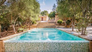 A rectangular pool with mosaic tile edges, surrounded by trees and a stone pathway leading to a building. - Beautiful home in Manacor with private swimming pool, can be inside or outside (Manacor)