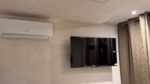 A room with a mounted flat-screen TV, an air conditioning unit, and a curtain. - WhatsApp  (Barcelona)