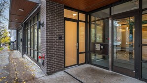 A modern building entrance with glass doors, a brick wall, and a wooden ceiling. - Roosevelt Suite| Walk to Light Rail + Rooftop View (Seattle)
