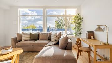A modern living room with a sectional sofa, a wooden desk, and a large window offering a city view.