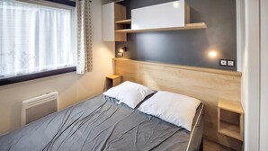 Een netjes opgemaakt slaapkamer met een bed, nachtkastjes, een verwarming en een raam met gordijnen.