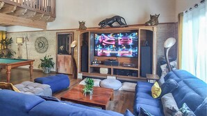Een woonkamer met een pooltafel, blauwe banken en een televisie op een houten standaard.
