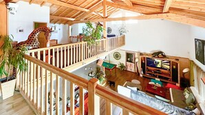 Een ruime woonkamer met een houten plafond, een girafsculptuur, een televisie en een biljarttafel.