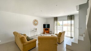 A spacious living room with two beige sofas, a coffee table, a TV on a wooden stand, and a large window with curtains. - Stunning home in Montignargues (Montignargues)