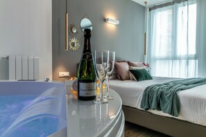 Ein modernes Schlafzimmer mit einem Bett, einem Nachttisch mit einer Flasche Veuve Clicquot Champagner und zwei Gl äsern, einem großen Fenster mit durchscheinenden Vorhängen und einem an der Wand befestigten Spiegel.