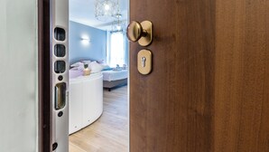 A hotel room with a wooden door, a white circular counter, a bed with a white headboard, and a hanging light fixture. - 4 Star Suite SPA  (Bologna)