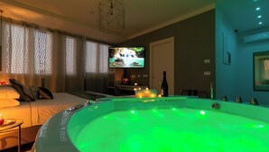 A room with a large, green-lit hot tub, a bed with pillows, a television on the wall, and a small table with candles. - 4 Star Suite SPA  (Bologna)