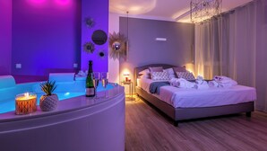 A modern hotel room with a large bed, a sitting area with a small pool, and a bar area with a pineapple and a bottle of champagne. - 4 Star Suite SPA  (Bologna)