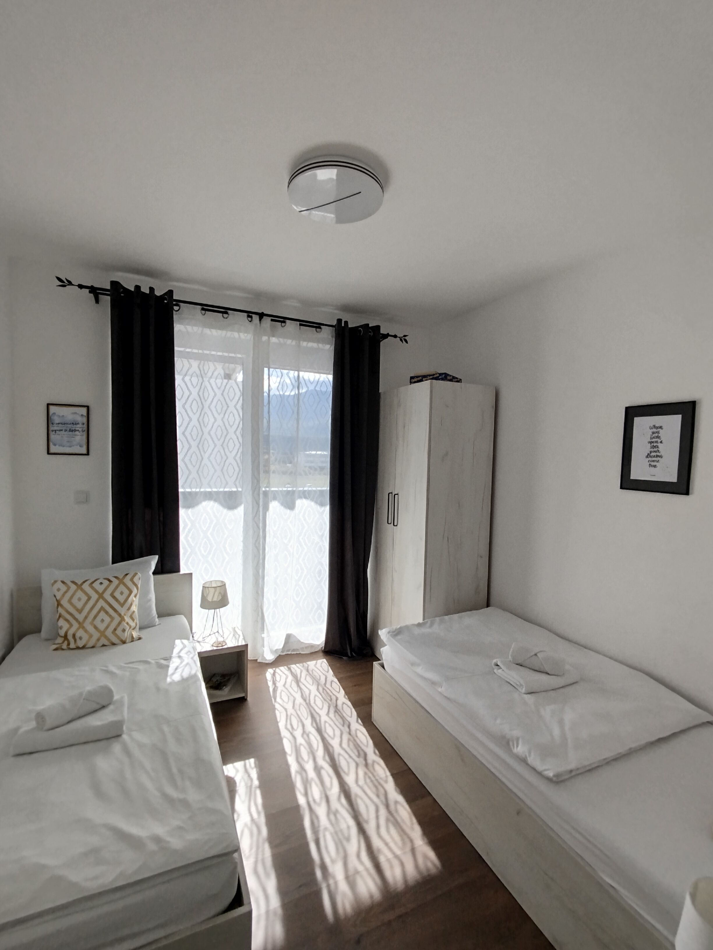A bedroom with two beds, a wardrobe, and a window with curtains.