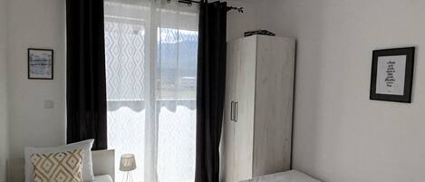 A bedroom with two beds, a wardrobe, and a window with curtains.