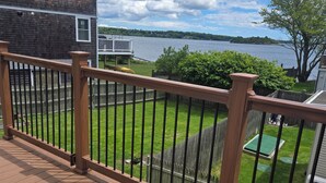 A wooden deck with a railing overlooking a grassy yard and a lake.