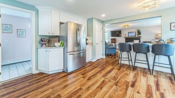 A modern kitchen with white cabinets, a stainless steel refrigerator, and a wooden floor.