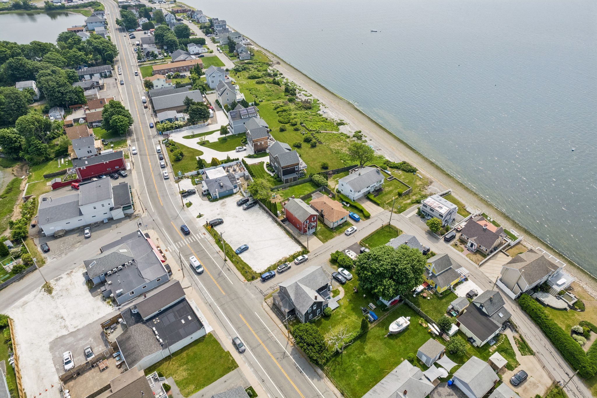 An aerial view of a coastal residential area with houses, a road, and a beach.