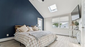 A bedroom with a bed, a skylight, a window, and a door.
