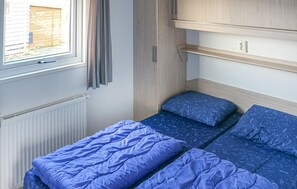 Une petite pièce comprenant un lit, une petite étagère et une fenêtre avec des rideaux.