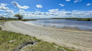 Ein weiter Sandstrand mit ruhigem Gewässer, blauem Himmel und vereinzelten Bäumen im Hintergrund.