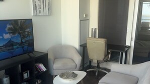 Un salon moderne avec un canapé blanc, un téléviseur, un lustre et un tableau accroché au mur.