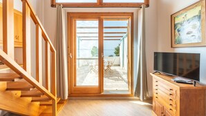 Ein Zimmer mit einer Holztreppe, einer Schiebeglastür, die zu einem Außenbereich führt, einem Holzkasten mit Fernseher und einem Gemälde an der Wand.