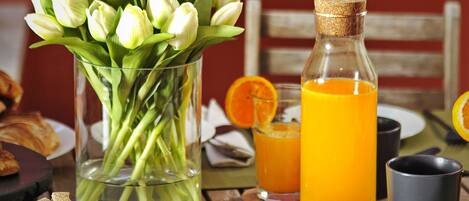 A breakfast setting with a vase of tulips, a bottle of orange juice, a bread basket, and a small bowl of cereal.